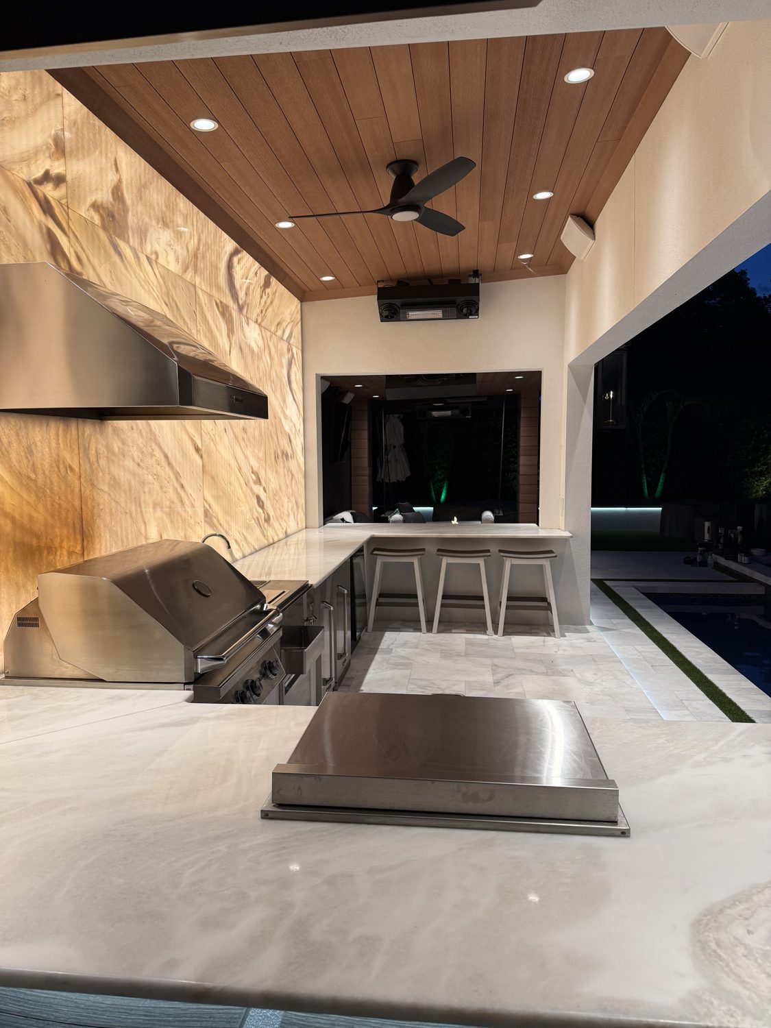 Custom outdoor kitchen with architectural recessed lighting and backlit stone feature wall